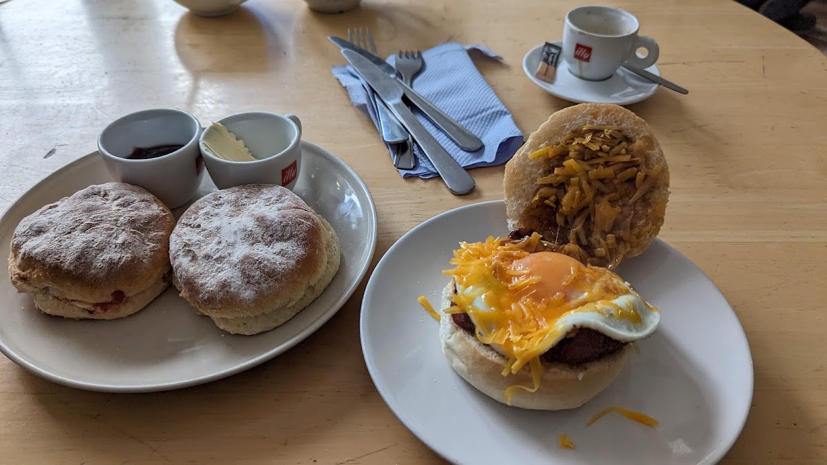 Two floury scones with jam and butter, beside a roll topped with a fried egg and grated cheddar, and an espresso.