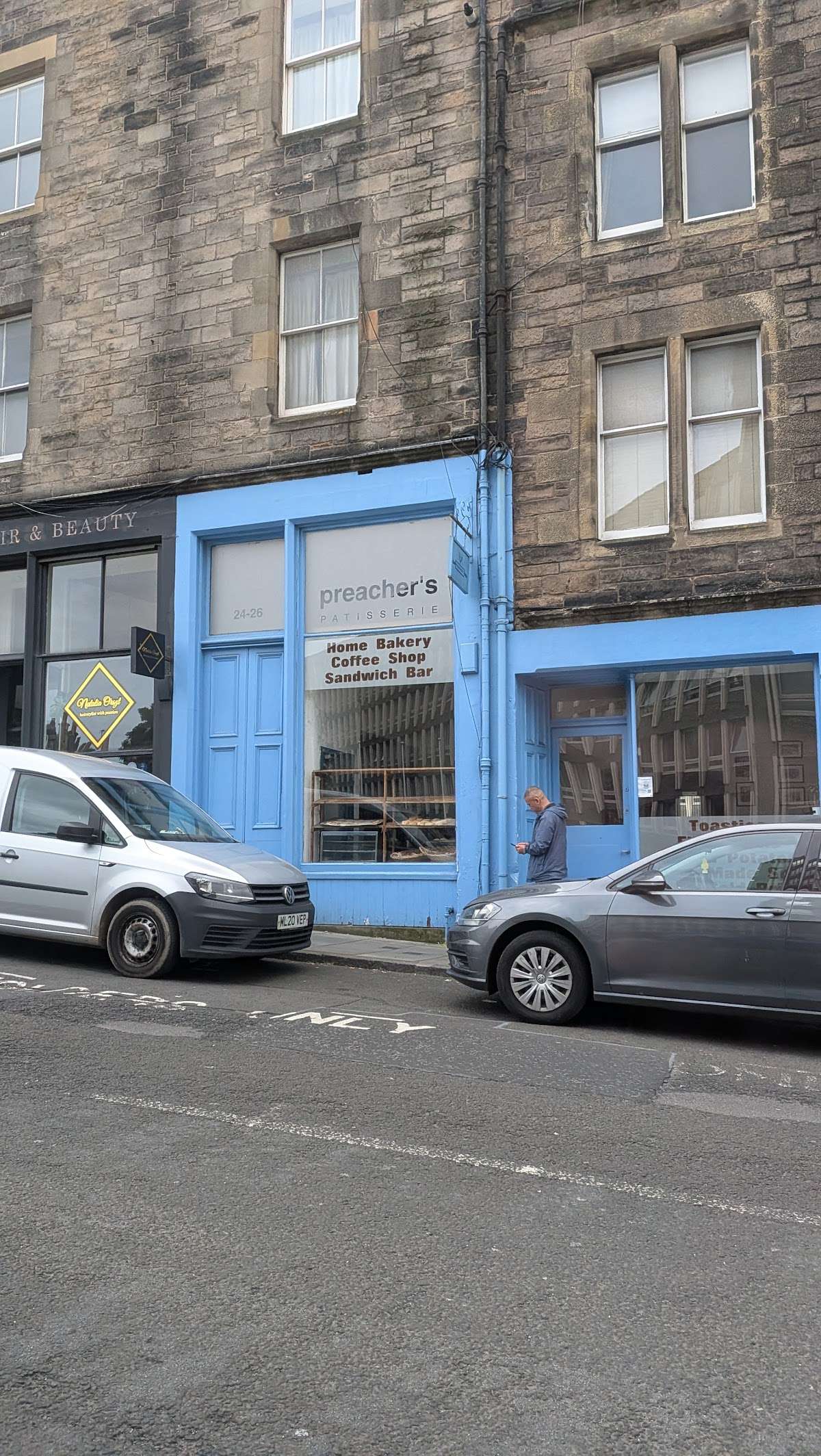 The shop from across Lady Lawson Street: a sky-blue painted frontage at 24-26 set into a grey sandstone tenement, with the window sign and racks of bakes inside.