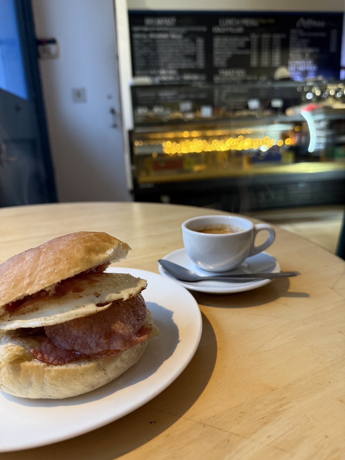 A bacon and fried egg roll with an espresso, the chalkboard menu and counter glowing in the background.
